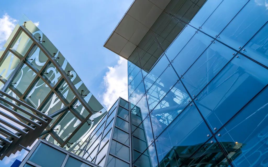 一座现代科技感的玻璃幕墙建筑，呈现几何线条与蓝色调