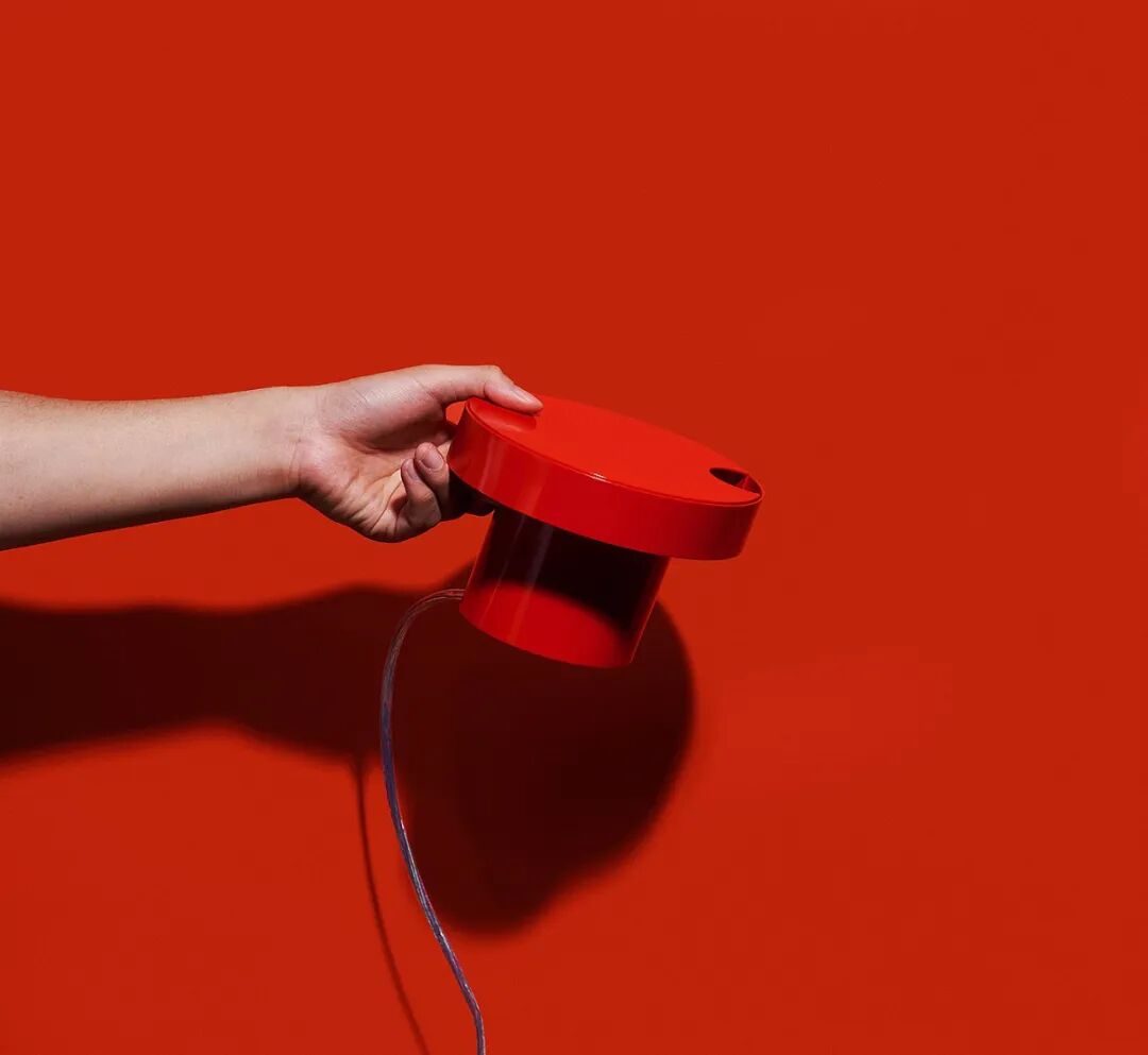 一只手握着一个红色的圆柱形设备，背景为纯红色