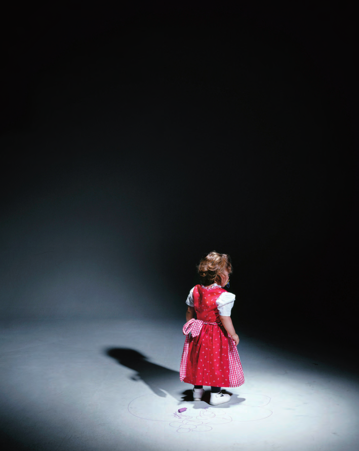 聚光灯下背对镜头穿红裙画画的小女孩
