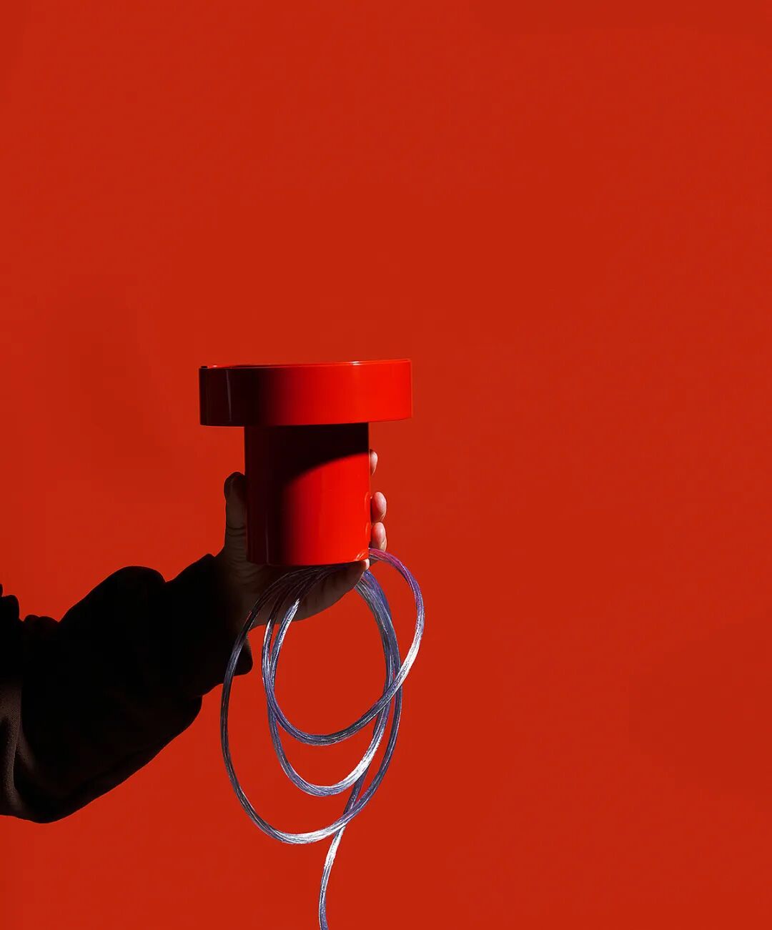 一只手握着一个红色的圆柱形物体，背景为纯红色