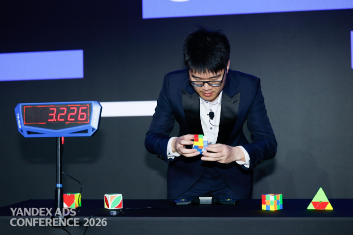 穿着西装的男性专注地转动魔方，桌面上有多个魔方和计时器