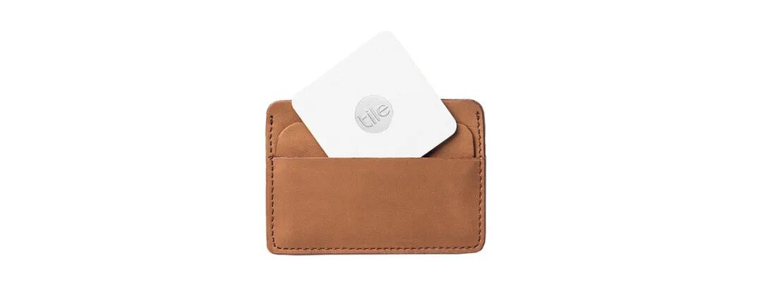 一个棕色皮革钱包，正面有一个卡槽，里面插着一个白色的Tile追踪器