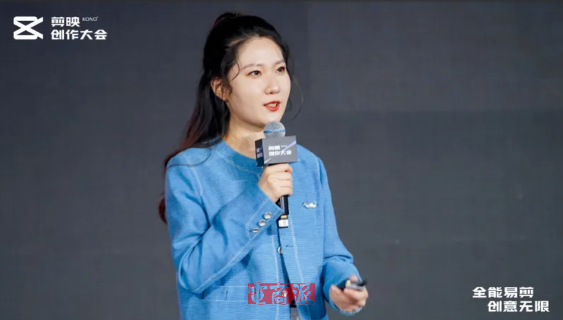身穿蓝色纹理西装外套的女性手持麦克风发言，背景为剪映创作大会标识